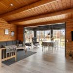 Wohn- und Essbereich mit Holzwand, Sofa, Tisch und großen Fenstern.