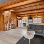 Wohnzimmer mit Küche und Holzdecke. Sofa, Couchtisch und Fernseher sichtbar.