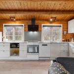 Küche mit weißen Schränken, Holzdecke und Fenstern zum Blick nach draußen.