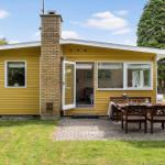 Gelbes Haus mit Terrasse, Tisch, Stühlen und Garten. Durchgangstür zu Wohnbereich.