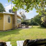 Gelbes Haus mit Garten, Terrasse und Sonnenschirm. Liegestühle im Vordergrund.