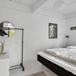 Schlafzimmer mit Bett, Kleiderständer und Fenster. Wände weiß, Boden hell.