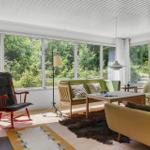 Ein Wohnzimmer mit großem Fenster, grünem Sofa, rotem Schaukelstuhl und Holzfußboden.