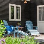 Terrasse mit blauen Stühlen, Tisch und Blumen vor schwarzem Holzhaus.