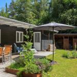 Haus mit Terrasse, Garten und Sonnenschirm. Tisch mit Stühlen und Pflanzen.