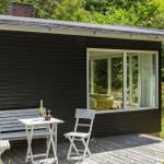 Schwarzes Holzhaus mit Terrasse, weißem Tisch und Stühlen, grüne Umgebung