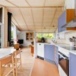 Küche mit blauen Schränken und Esstisch. Holzdecke und große Fenster.
