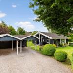 Schwarzes Haus mit Carport, Grasfläche und Bäumen.