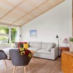 Wohnzimmer mit Sofa, zwei Stühlen und Holzboden. Große Fenster und Holzdecke.