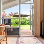 Raum mit Holzfußboden, Kamin und Terrassentür zur grünen Außenterrasse.
