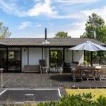Haus mit Terrasse, Grill und Sitzgruppe unter Sonnenschutz.