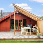 Rotes Holzhaus mit Terrasse, Grill und Sitzgelegenheiten unter einem Dach.