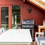 Roter Holzausenaufenthalt mit Grill, Tisch und Bank.