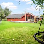 Roter Holzausstattungshaus mit Terrasse, Trampolin und Schaukel im Garten.