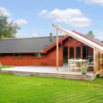 Rotes Ferienhaus mit Holzterrasse und Grillplatz im Grünen.