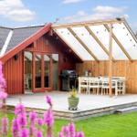 Roter Holzhaus mit Terrasse, Grill und weißem Tischset im Garten.
