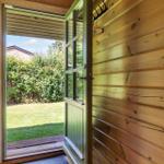 Holzverkleidete Türöffnung zum Garten mit Rasen und Hecke.