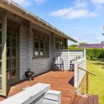 Terrasse mit Grill und Stühlen vor einem Haus mit Holzfassade.