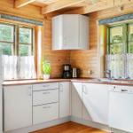 Küche mit weißen Schränken, Holzwänden und Fenstern mit Vorhängen.