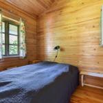 Schlafzimmer mit Holzwand, Bett, Fenster mit Vorhängen und Wandlampe.