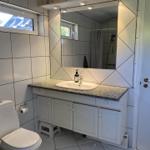 Badezimmer mit Waschbecken, Spiegel und Toilette. Fliesenwand und Fenster sichtbar.