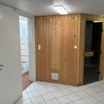 Sauna mit Holzwand und Tür im Raum mit Fliesenboden.