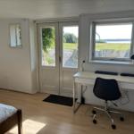 Zimmer mit Schreibtisch, Bett und Blick auf Grünland und Wasser.