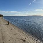 Strand mit Sand und Wasser unter blauem Himmel mit wenigen Wolken.