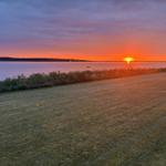 Sonnenuntergang über See mit Booten und Grasfläche im Vordergrund.