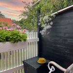 Terrasse mit Blumenkasten, Tisch und Stuhl. Blick auf Garten und Himmel.
