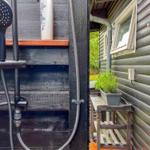 Außen-Dusche mit Handdusche und Pflanze auf Holzgestell.