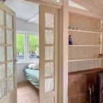 Durchgehende Tür führt in ein Schlafzimmer mit Bett und Fenster. Nebenher steht ein Kamin mit Regalen.