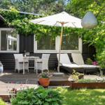 Terrasse mit Tisch, Stühlen, Liegen und Sonnenschirm. Umgeben von Pflanzen und Grün.