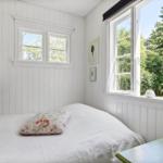 Schlafzimmer mit weißer Wandverkleidung, Bett und Fenster mit Blick auf Bäume.