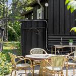 Außenbereich mit Tisch und Stühlen vor einem schwarz gestrichenen Holzhaus mit Gartentüren.