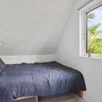 Schlafzimmer mit Dachschräge, Bett und Fensterblick auf Bäume.