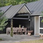 Schwarze Holzhütte mit Terrasse, Tisch und Stühlen. Eingangstür und Pflanzen sind sichtbar.