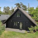 Schwarzes Holzhaus mit Dachterrasse und Garten. Umgeben von Bäumen und Grün.