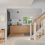 Küche mit Holzschrank und Fenster. Treppe mit Holzgeländer. Holzboden und weiße Wände.