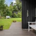 Haus mit Terrasse, Garten und weißer Bank. Pflanzen und Steinzaun sind sichtbar.