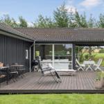 Holzterrasse mit Sitzgelegenheiten und Grill. Blick auf grüne Wiese und Bäume.