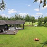 Haus mit Terrasse, Grill, Liegestühlen und Feuerkorb auf grünem Rasen.