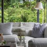 Sitzbereich mit Sofa und Kissen vor großem Fenster mit Blick auf Garten.