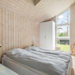 Schlafzimmer mit Holzwand, Bett, Kleiderschrank und Sicht auf Garten.