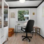 Schreibtisch mit Stuhl und Fenster, daneben Glaswand und Stühle.