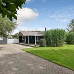 Ein Haus mit Terrasse, Rasen und hohem Gras. Pflasterweg führt zur Eingangstür.