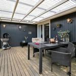 Terrasse mit Grill, Tisch und Stühlen unter Dach.