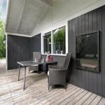 Terrasse mit Tisch und Stühlen, schwarze Holzwände und großes Fenster.