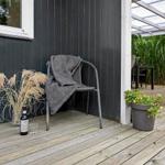 Terrasse mit Stuhl, Decke, Pflanzen und Weinflasche neben Hauswand.