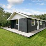 Moderne Hütte mit Holzterrasse und grünem Garten. Fenster und Tür sind weiß.